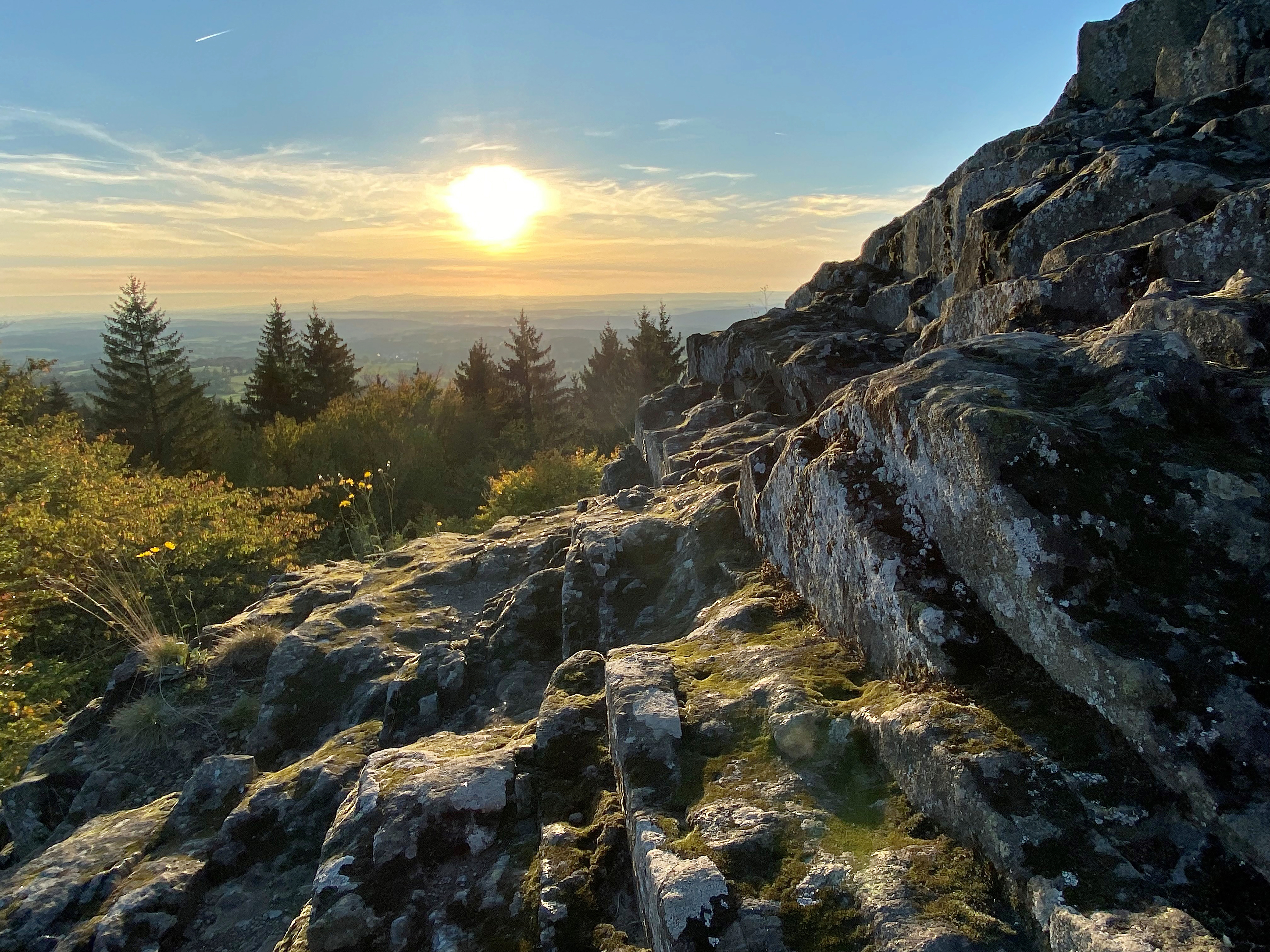 Der Blick vom schroffen Basaltfelsen des Geotopes Bilstein im hessischen Vogelsberg geht weit über das geschwungene Land der Vulkanregion. Der Herbst hat das Laub des Waldes bunt gefärbt und die warmen Sonnestrahlen zaubern ein magisches Licht am strahlend blauen Himmel.
